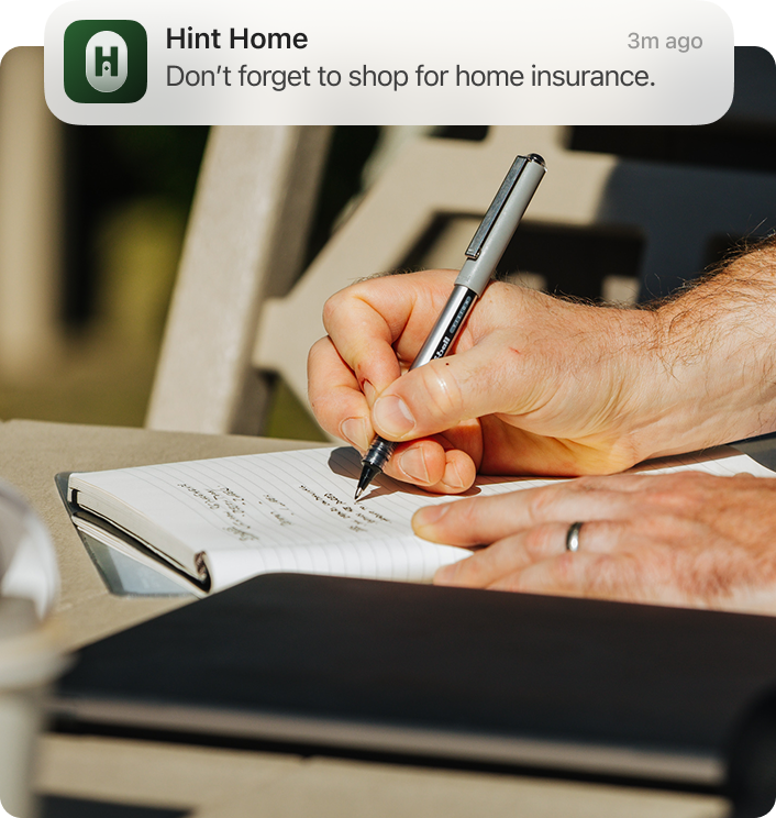 Hands writing in a notebook with a Hint Home notification about home insurance