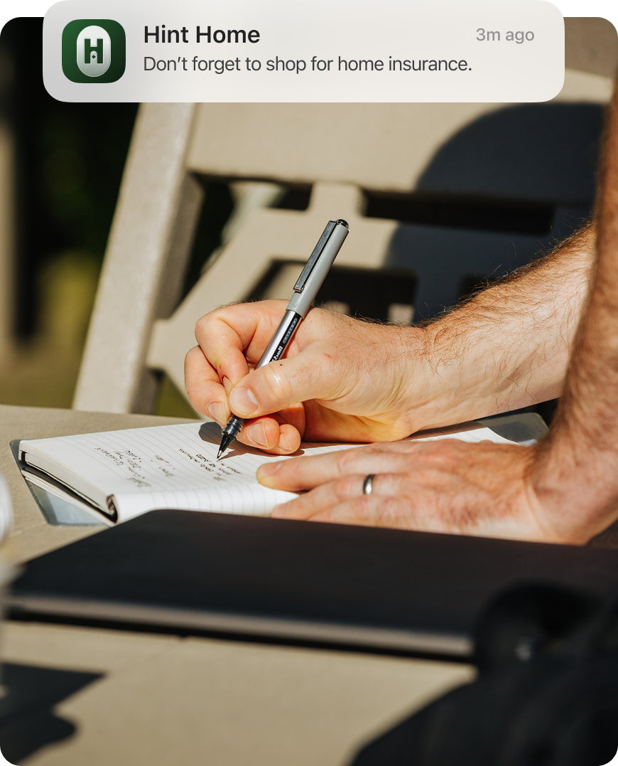 Hands writing in a notebook with a Hint Home notification about home insurance